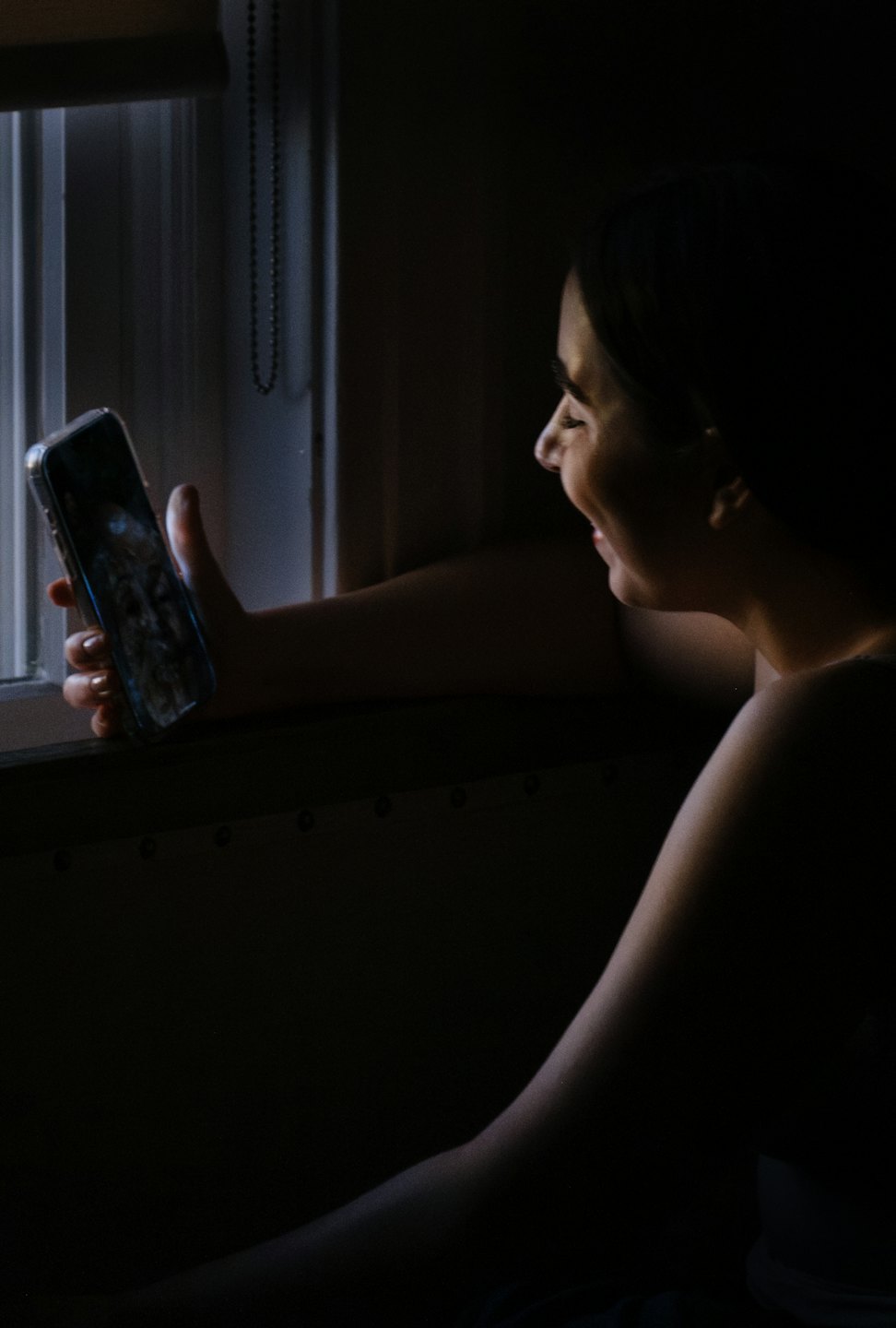 Egy személy mosolyogva néz a telefonjára egy beltéri felvételen.