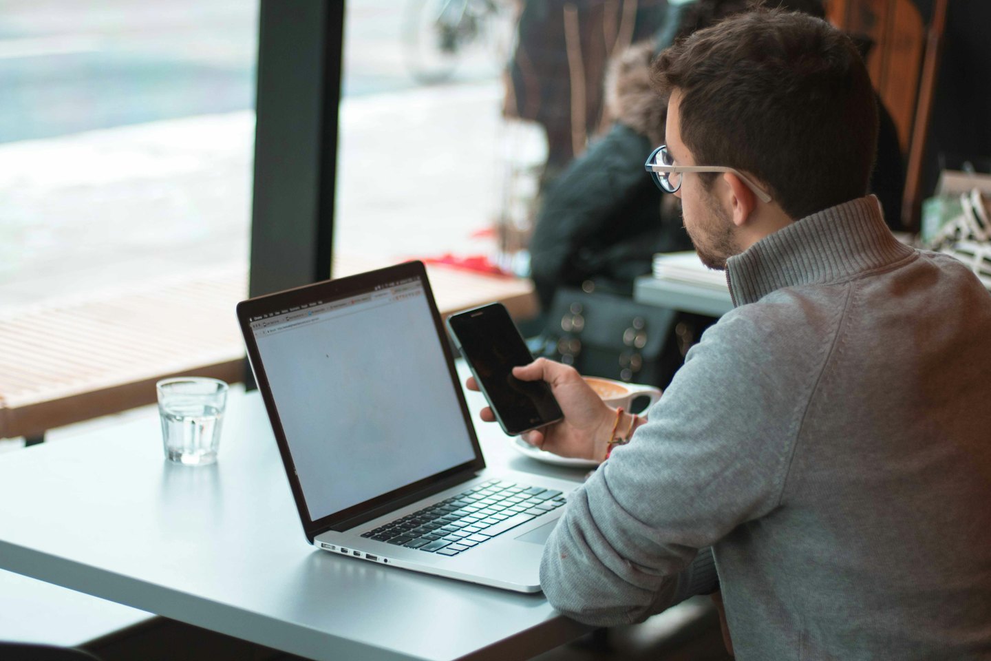 Férfi dolgozik laptopon egy kávézó asztalánál okostelefonnal.
